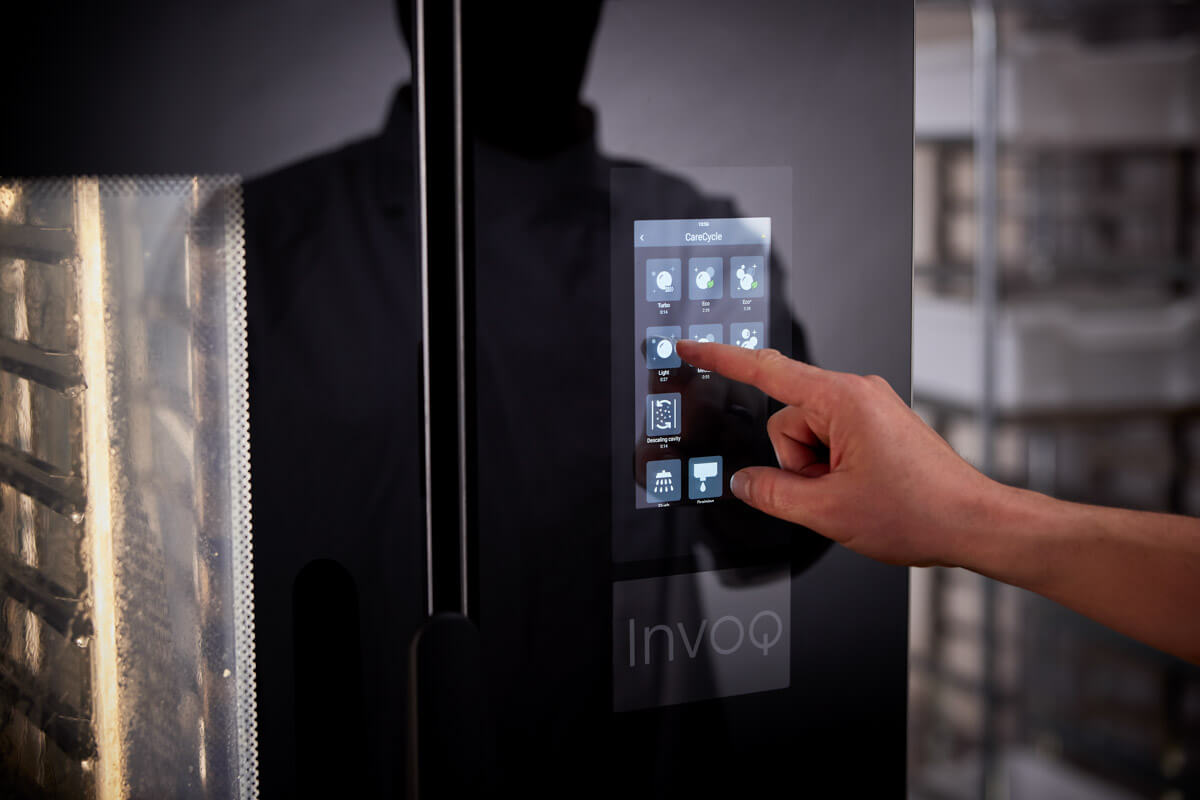 Un professionnel de la cuisine utilisant un four Invoq Combi et Hybrid pour préparer des plats frais et de grande qualité grâce à une interface tactile intuitive.